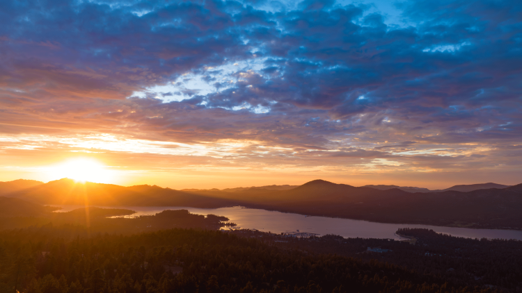A picture of a bright orange sunset peaking out from above the mountains in Big Bear Lake California.