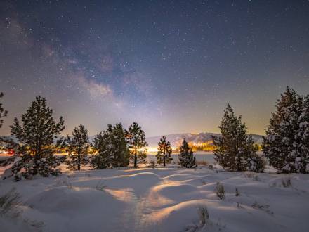 A photo of Big Bear's night sky taken during winter after a snowfall, the bright stars and a galaxy are visible.