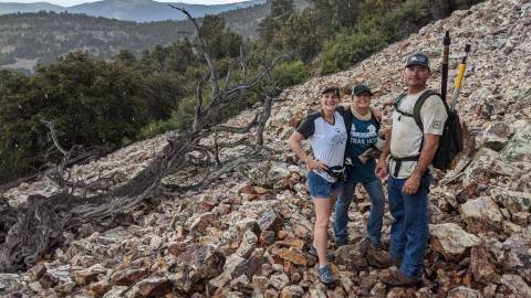 A photo of volunteers on a rocky hill, one of them is carrying a backpack with long tool like sticks.