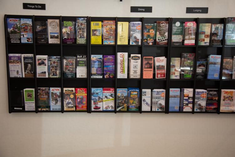 A photo of the Big Bear Visitor Center wall of brochures, there are categories for dining, things to do, and lodging.